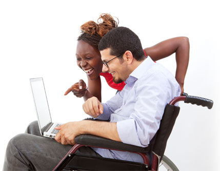 Young woman with young man in a wheelchair, holding a laptop.